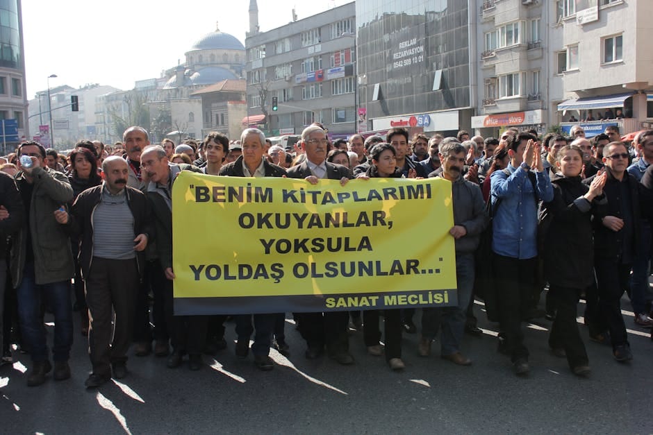 A diverse crowd protesting in an urban area, holding a notable banner.