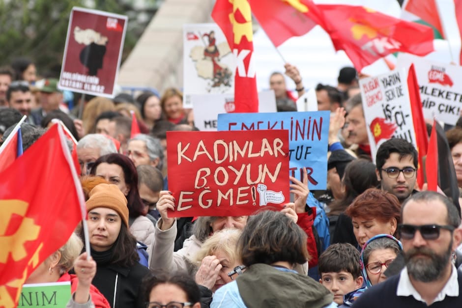 A diverse group of people in a protest holding signs and red flags, advocating for social issues.