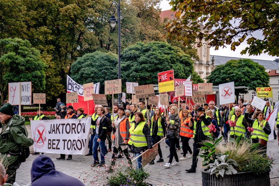 A large group protests in Warsaw's city center, holding placards with messages in Polish.