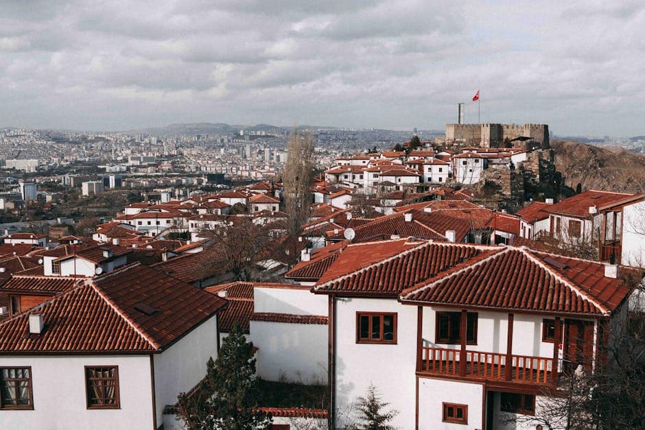 Aerial view of Ankara's traditional red rooftops and historic castle under a cloudy sky.
