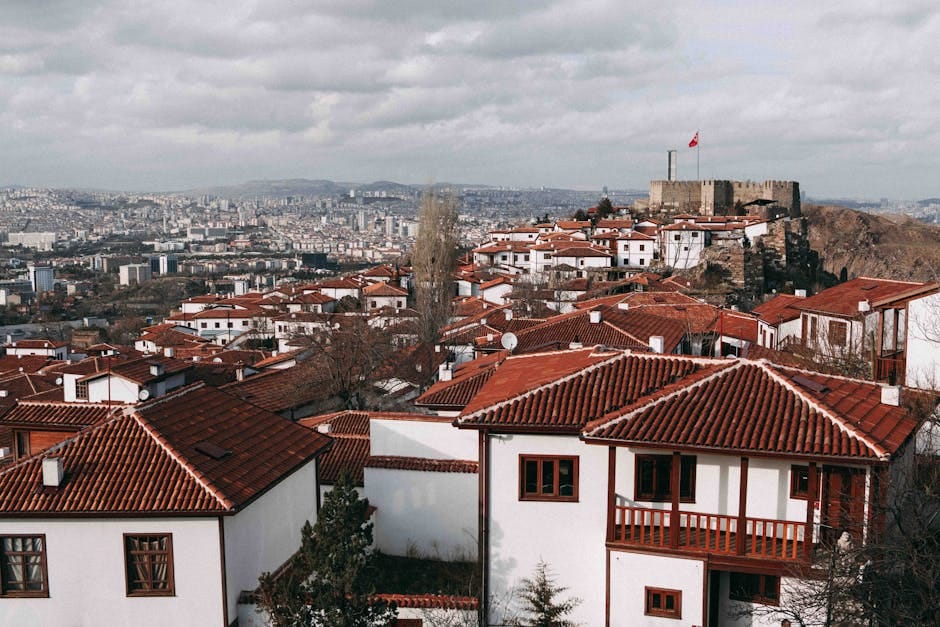 Aerial view of Ankara's traditional red rooftops and historic castle under a cloudy sky.