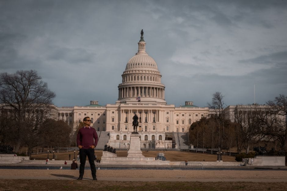 Person standing in front of the iconic United States Capitol on a clear day.