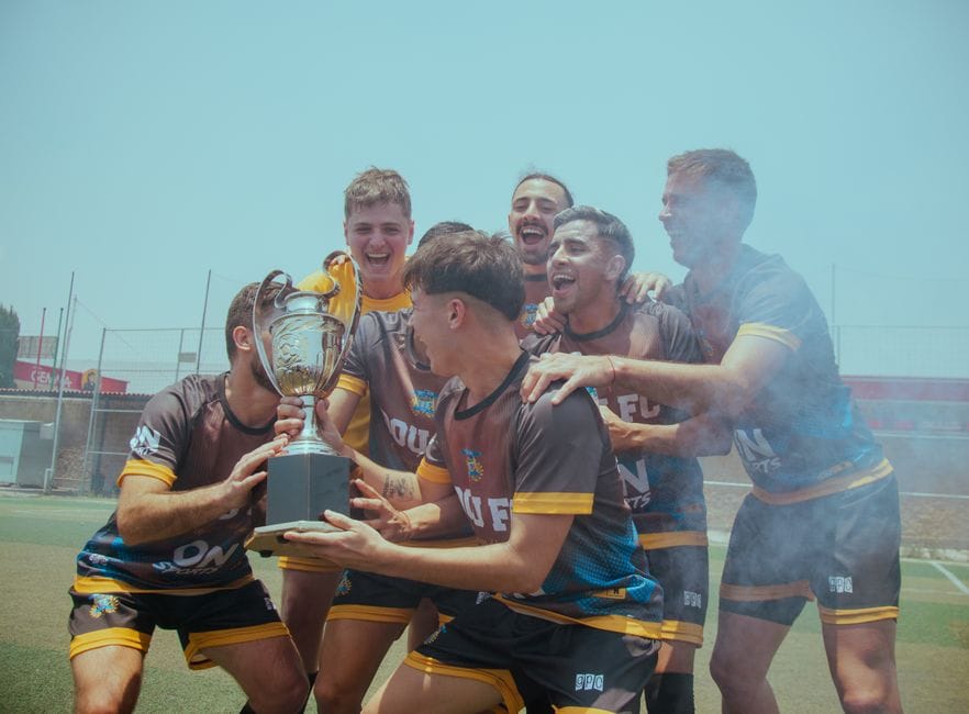 A joyful sports team celebrating their victory with a trophy outdoors on a sunny day.