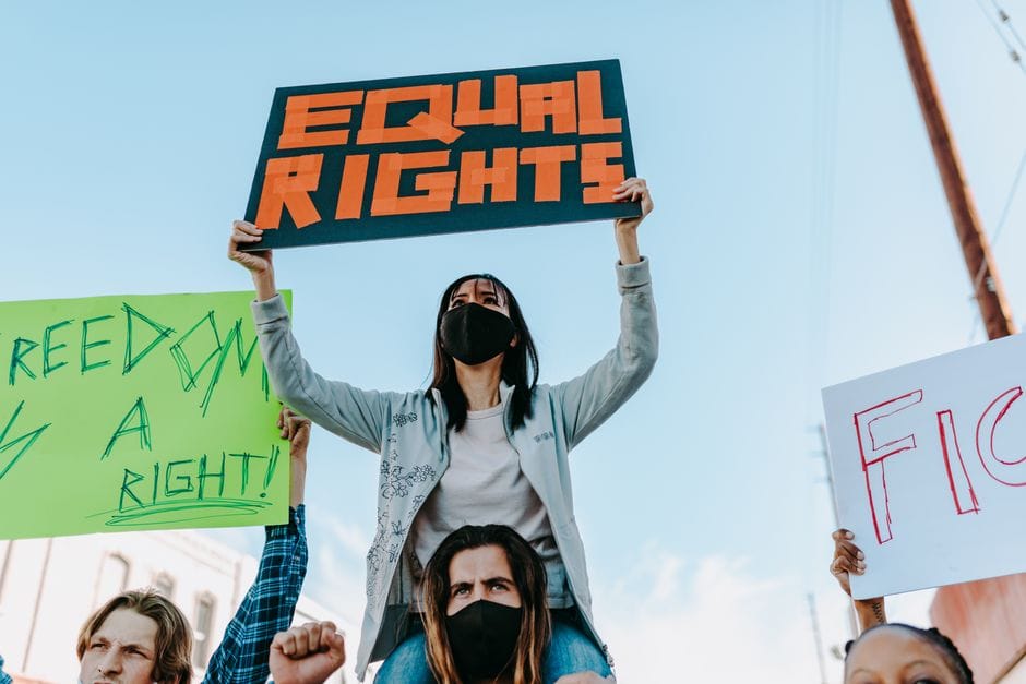 Masked protesters holding signs advocating for equal rights in an outdoor demonstration.