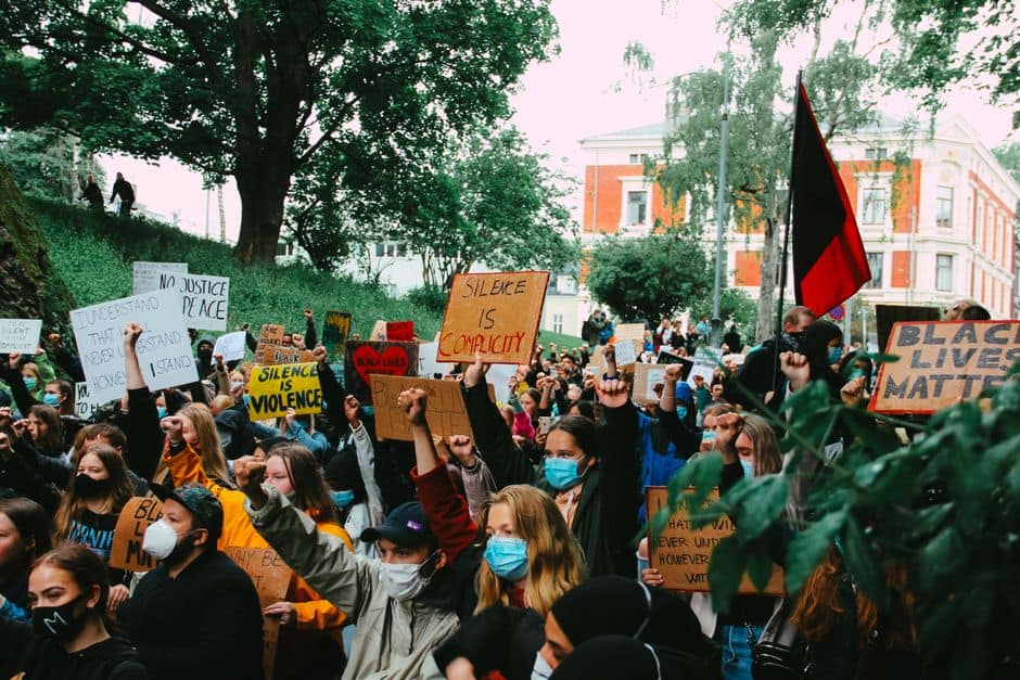 A crowd of diverse protesters holding signs and wearing masks in a peaceful Black Lives Matter rally.