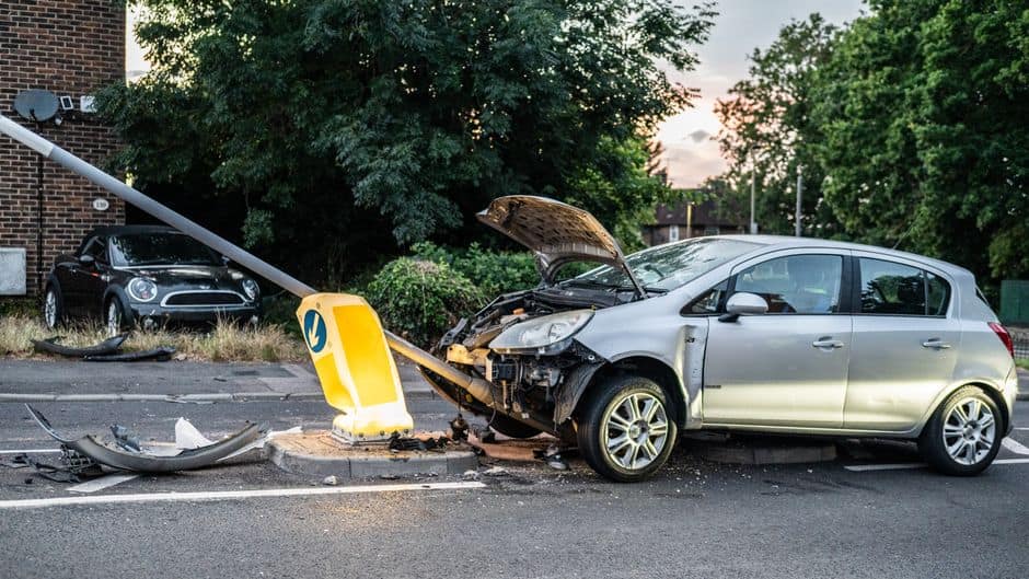 A damaged car that crashed into a lamp post on a London street during twilight.