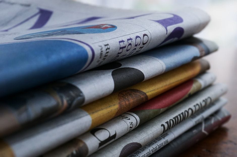 Close-up of a stack of colorful newspapers on a wooden table, showcasing print media.