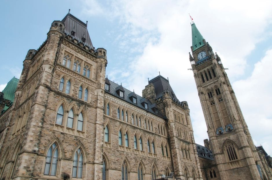 A view of the historical Parliament Hill building in Ottawa against a clear sky.