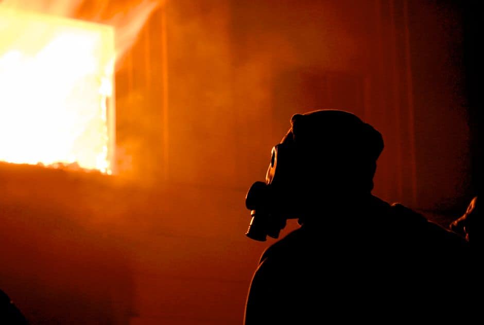Eerie silhouette of a person with a gas mask in profile, facing intense flames and smoke.