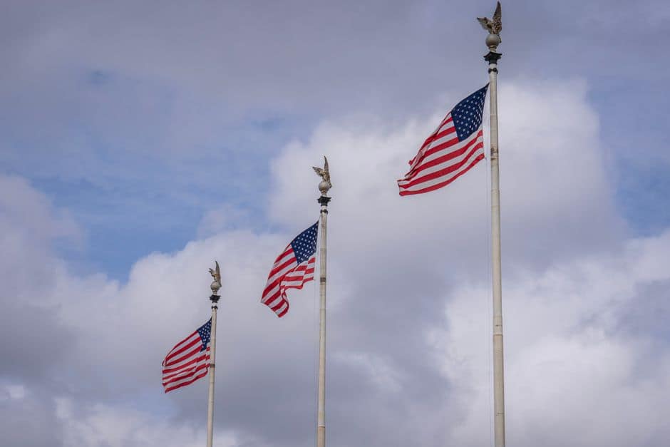 Three American flags waving against a backdrop of fluffy clouds, symbolizing national pride.