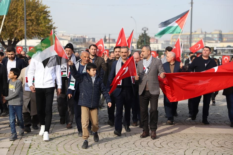 A protest march with participants waving Turkish and Palestinian flags outdoors.