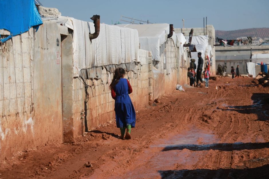 Back view of anonymous girl strolling on dirty ground near brick constructions with chimneys
