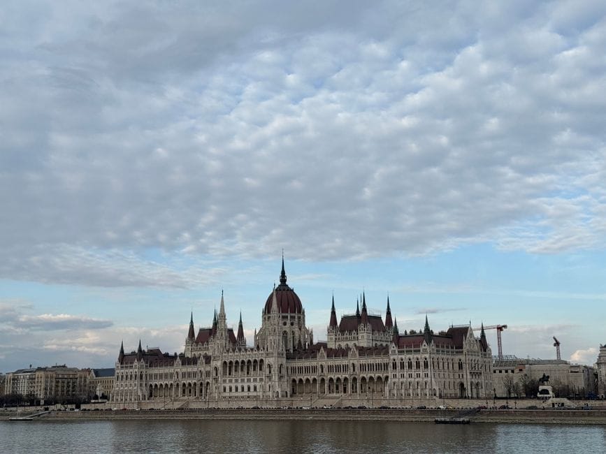Scenic view of the Hungarian Parliament Building by the river under a cloudy sky in Budapest.