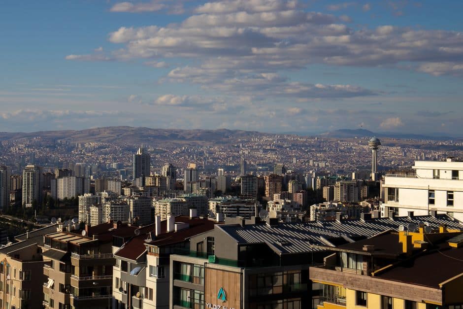 A sweeping aerial view of Ankara's cityscape under a bright, cloudy sky.