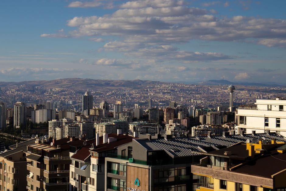 A sweeping aerial view of Ankara's cityscape under a bright, cloudy sky.