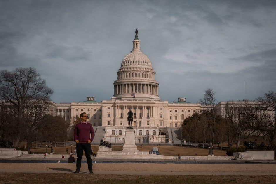Person standing in front of the iconic United States Capitol on a clear day.