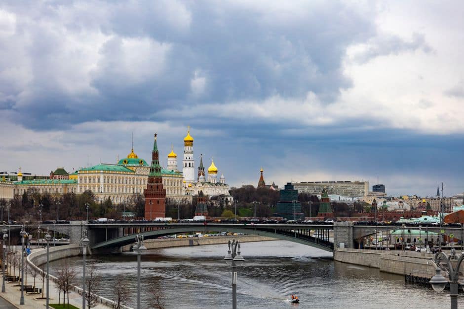 A picturesque view of the Moscow Kremlin with a bridge over the Moskva River under a dramatic sky.