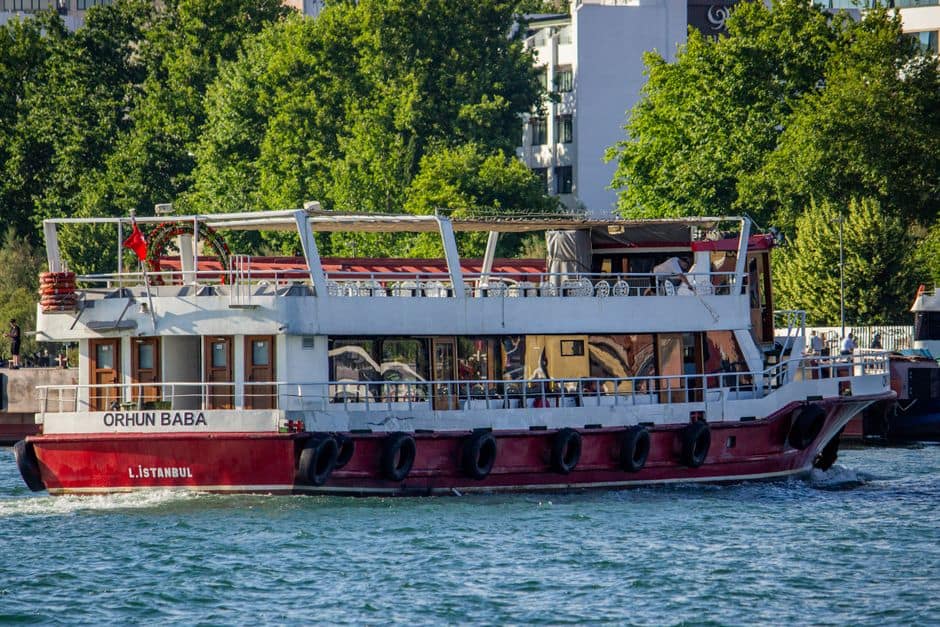 A vibrant red ferry boat travels along Istanbul's waterfront on a sunny day.