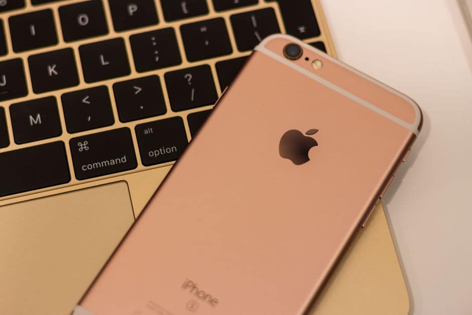 Close-up of a rose gold iPhone 6s placed on a MacBook keyboard, showcasing sleek design and modern technology.