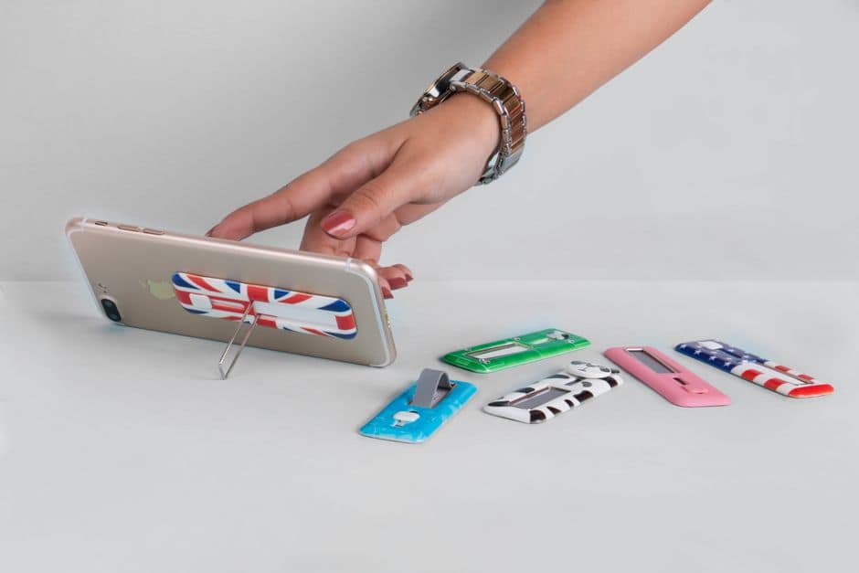Female hand using a smartphone stand with various decorative designs on a table.