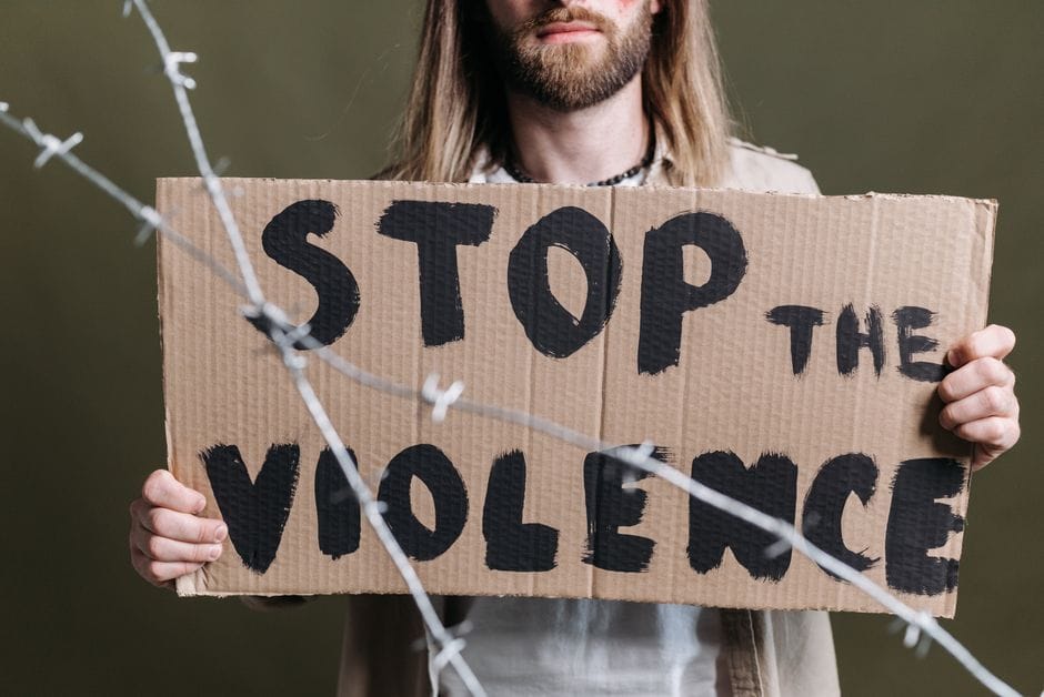 Close-up of a protester holding a cardboard sign reading 'Stop the Violence' with barb wire in focus.
