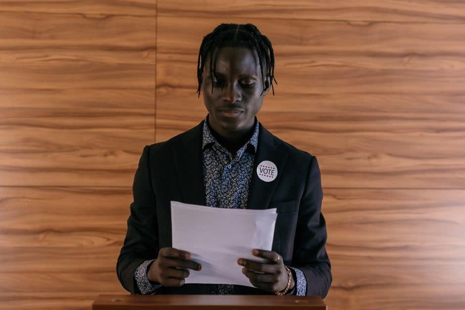 Black man wearing a suit addressing a document, possibly in a political setting.