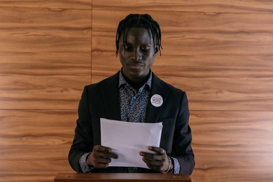 Black man wearing a suit addressing a document, possibly in a political setting.