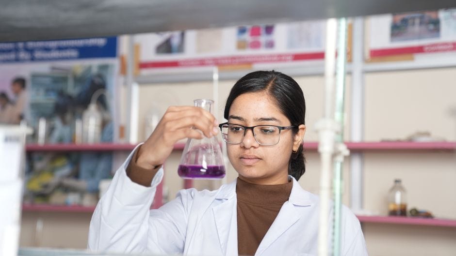 Female scientist examining a purple chemical solution in a laboratory setting.