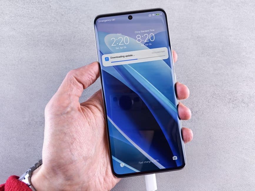 Close-up of a hand holding a smartphone with a downloading update notification on the screen.