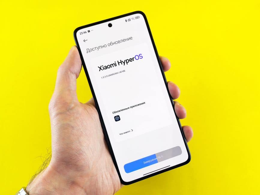 Hand holding smartphone showing Xiaomi HyperOS update screen on yellow background.